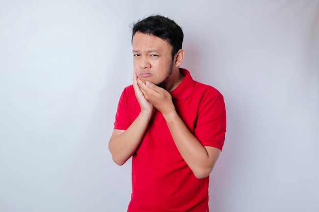 Un portrait d'un homme asiatique portant un t-shirt rouge isolé sur fond blanc a l'air déprimé