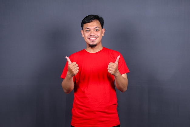 Portrait d'un homme asiatique séduisant en chemise rouge debout avec bras croisé isolé sur fond gris