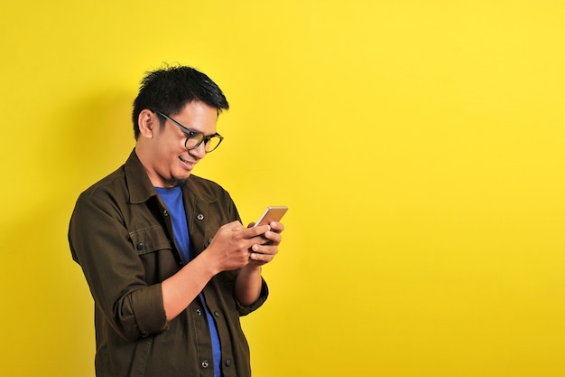Portrait d'un homme asiatique souriant et heureux utilisant un smartphone portant un t-shirt décontracté et une veste avec des lunettes, obtenez le meilleur prix, en utilisant un simple paiement bancaire mobile