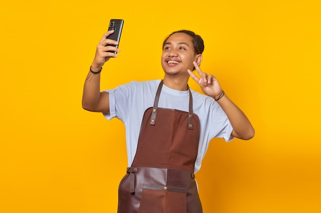 Portrait d'un homme asiatique souriant et montrant un signe de paix tout en prenant un selfie sur un téléphone portable