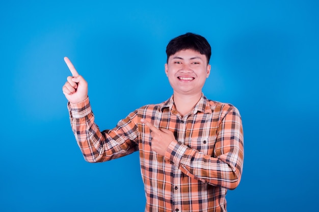 Portrait d'un homme asiatique souriant porter une chemise pointant le doigt sur le côté sur fond bleu