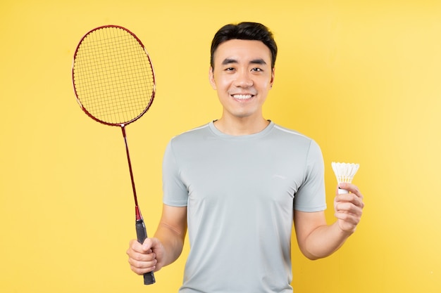 Portrait d'un homme asiatique tenant une raquette de badminton sur un mur jaune