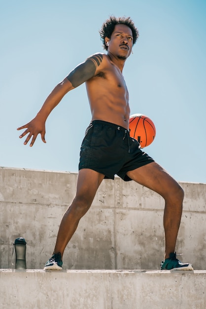 Portrait d'un homme athlète afro jouant et pratiquant avec un ballon de basket à l'extérieur. Sport et mode de vie sain.