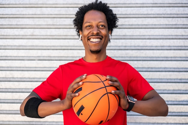 Portrait de l'homme athlète afro tenant un ballon de basket en se tenant debout à l'extérieur