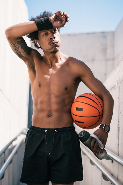 Portrait d'homme athlète tenant un ballon de basket et se détendre après l'entraînement en plein air