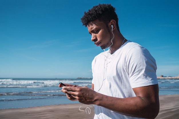 Portrait d'un homme athlétique à l'aide de son téléphone portable lors d'une pause d'entraînement sur la plage. Mode de vie sport et santé.