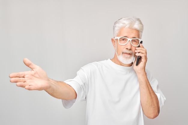 Photo portrait d'un homme aux cheveux gris en t-shirt blanc parlant au téléphone portable une personne avec un smartphone isolé sur un fond blanc