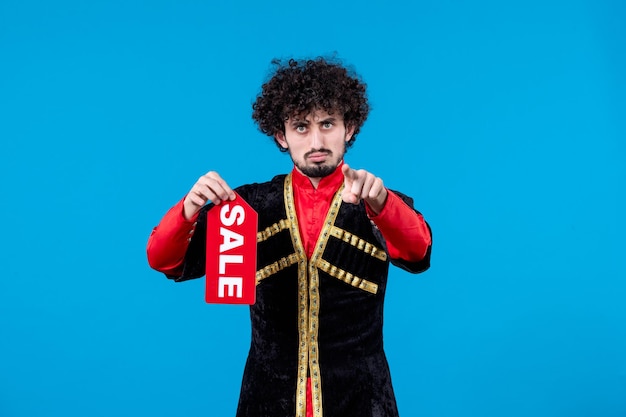 Portrait d'un homme azéri en costume traditionnel tenant une plaque signalétique de vente sur fond bleu couleur ethnique novruz shopping printemps