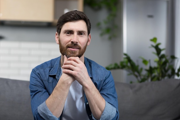 Portrait d'un homme avec une barbe à la maison assis sur le canapé et regardant la caméra