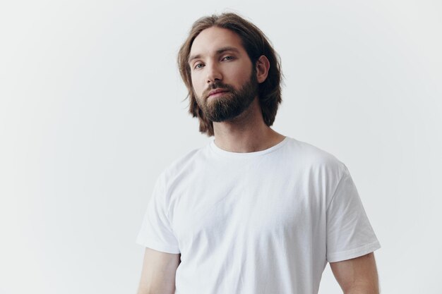 Portrait d'un homme avec une barbe noire épaisse et de longs cheveux dans un T-shirt blanc sur un fond blanc isolé émotion de tristesse et de nostalgie