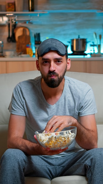 Portrait d'homme à la barbe tenant un bol de pop-corn tout en regardant un film de divertissement à la télévision