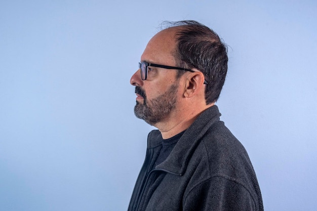 Portrait d'un homme barbu de 60 ans sur fond bleu avec chapeau et lunettes