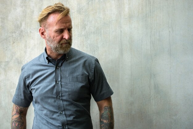 Portrait d'homme barbu beau mature avec des tatouages à la main contre le mur de béton à l'extérieur