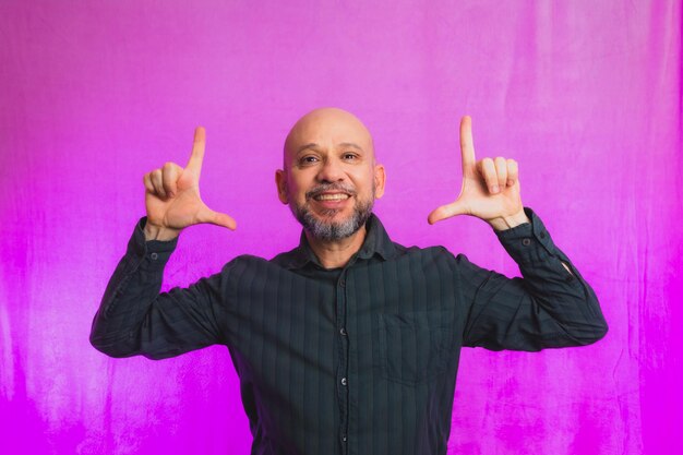 Portrait d'un homme barbu et chauve faisant des signes avec les mains isolées sur fond rose