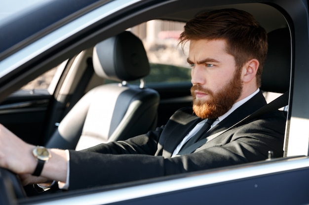 Portrait d'un homme barbu concentré en costume au volant de voiture