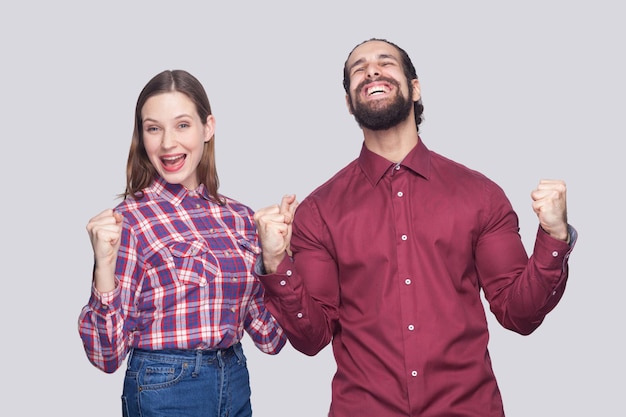 Portrait d'un homme barbu heureux et étonné avec des cheveux noirs et une femme dans un style décontracté debout avec le poing et célébrant leur victoire. tourné en studio intérieur, isolé sur fond gris.