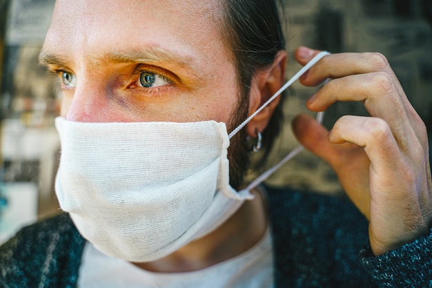 Portrait d'un homme barbu met un masque de gaze avant de quitter la maison. Lutte préventive contre l'infection virale - coronavirus COVID-19. Concept de protection de la santé