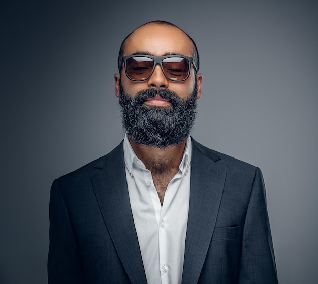 Portrait d'un homme barbu à la mode en costume et lunettes de soleil isolé sur fond gris.