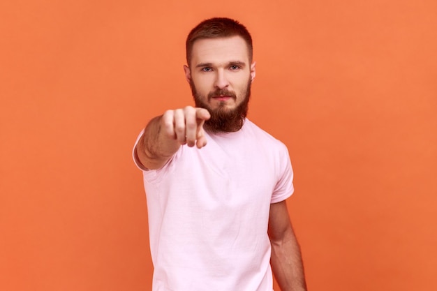 Portrait d'un homme barbu réprimandant pour erreur insatisfait du comportement blâmant montrant un geste d'avertissement portant un t-shirt rose Studio tourné en intérieur isolé sur fond orange