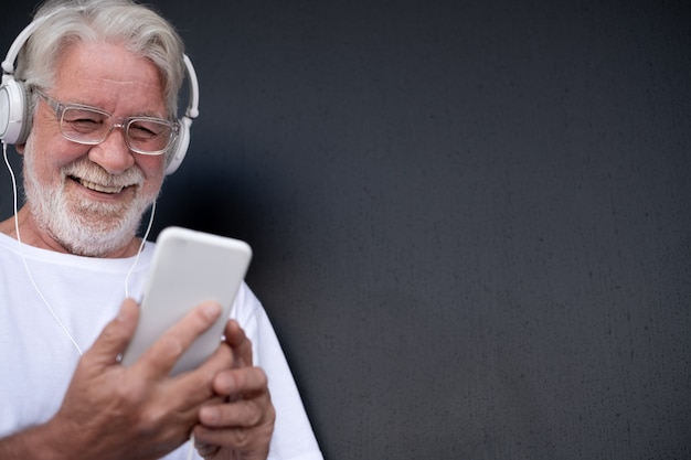 Portrait d'un homme barbu senior souriant tout en écoutant de la musique par téléphone intelligent Casque blanc