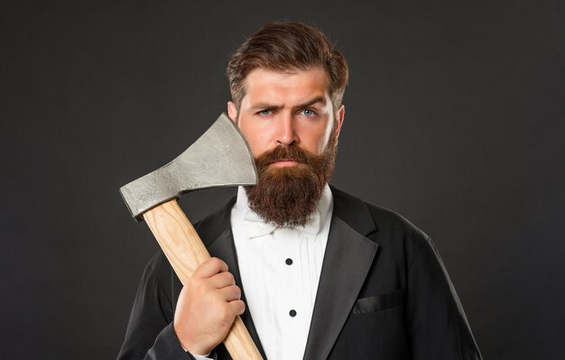 Portrait d'un homme barbu sérieux tenant une hache au fond sombre du visage non rasé, salon de coiffure