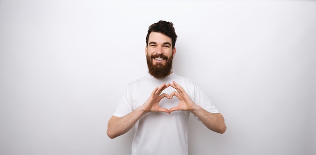 Portrait d'homme barbu souriant faisant le symbole du cœur sur fond blanc