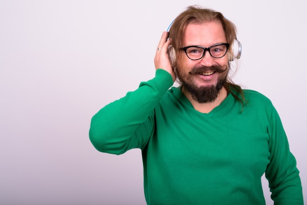 Portrait d'homme barbu en surpoids avec moustache et cheveux longs portant un pull vert contre le mur blanc