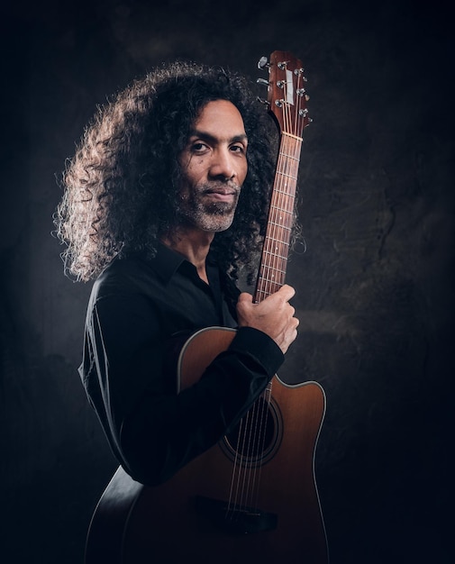 Photo portrait d'un homme bouclé attrayant avec guitare au studio photo sombre.