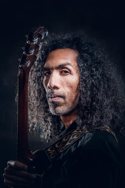 Portrait d'un homme bouclé attrayant avec guitare au studio photo sombre.