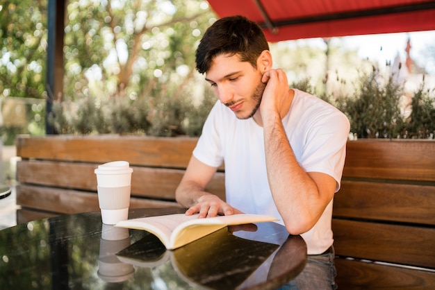 Portrait d'un homme caucasien bénéficiant de temps libre et lisant un livre assis à l'extérieur au café. Concept de mode de vie.