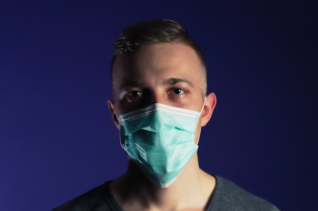 Portrait d'homme caucasien dans un masque de gaze médical sur fond bleu foncé. Concept de prévention des virus.