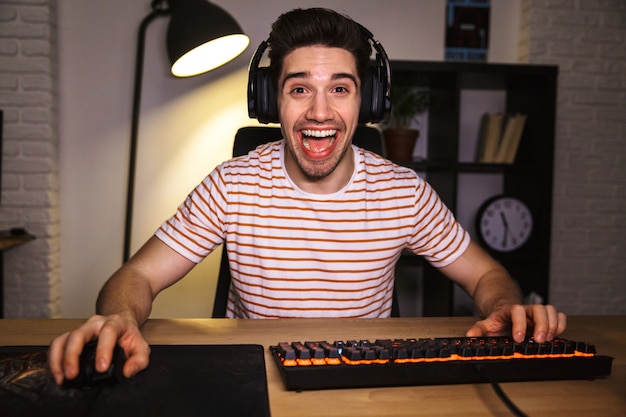 Portrait d'un homme caucasien portant des écouteurs souriant tout en regardant sur l'ordinateur, et à l'aide d'un clavier coloré rétroéclairé