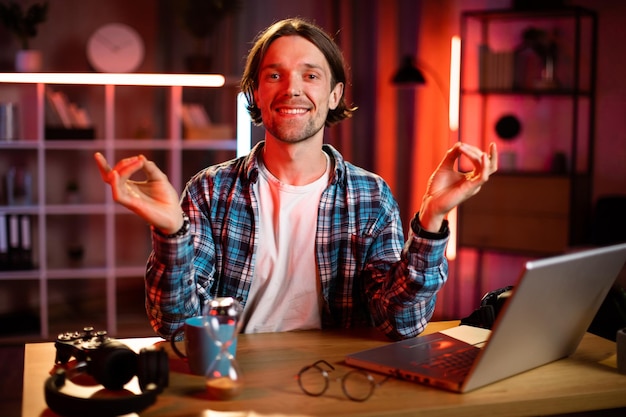 Photo portrait d'un homme caucasien souriant en chemise pratiquant des exercices de yoga pendant la soirée à la maison