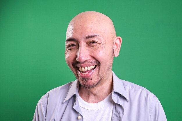 Portrait d'un homme chauve asiatique souriant sur un fond vert