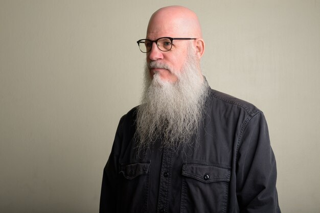 Portrait d'homme chauve mature avec une longue barbe grise contre un mur blanc