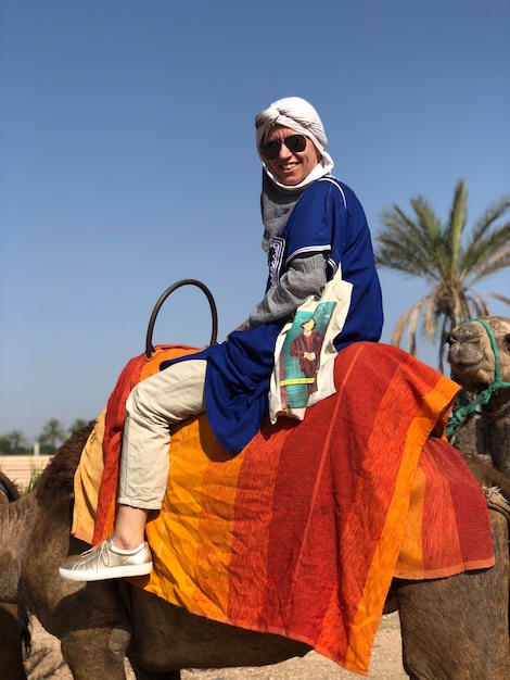 Photo portrait d'un homme à cheval sur un chameau contre un ciel bleu clair