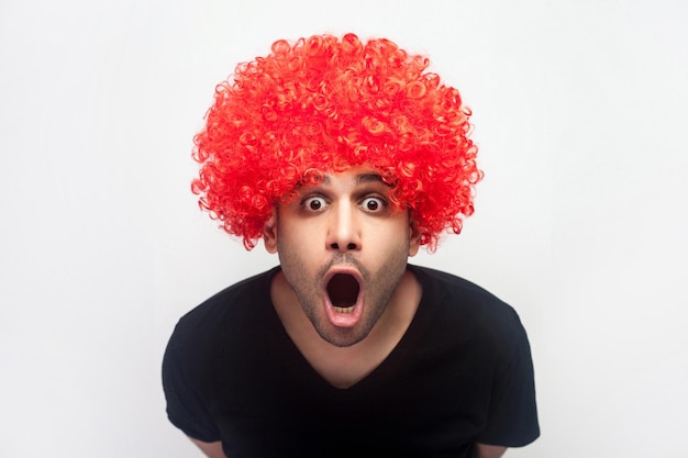 Portrait d'un homme choqué accablé avec des poils et une perruque rouge regardant avec surprise la caméra, criant d'étonnement et de joie, réaction d'incrédulité. studio d'intérieur tourné isolé sur fond blanc