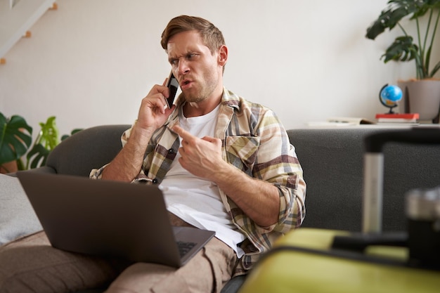 Portrait d'un homme en colère se disputant au téléphone a l'ordinateur portable ouvert sur son ordinateur portable est assis près de la valise