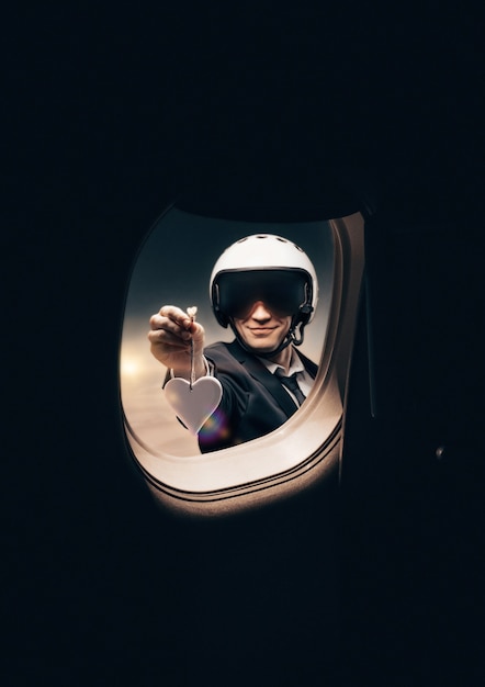 Portrait d'un homme dans un casque. Il regarde dans le hublot d'un avion et lui tend une silhouette en forme de cœur. Concept de voyage et d'assurance.