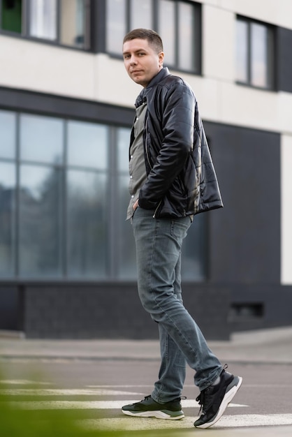 Portrait d'un homme dans une veste noire et un jean regardant la caméra traversant la rue