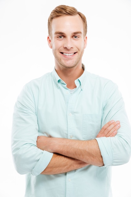 Portrait d'un homme décontracté heureux debout avec les bras croisés sur un mur blanc et regardant à l'avant