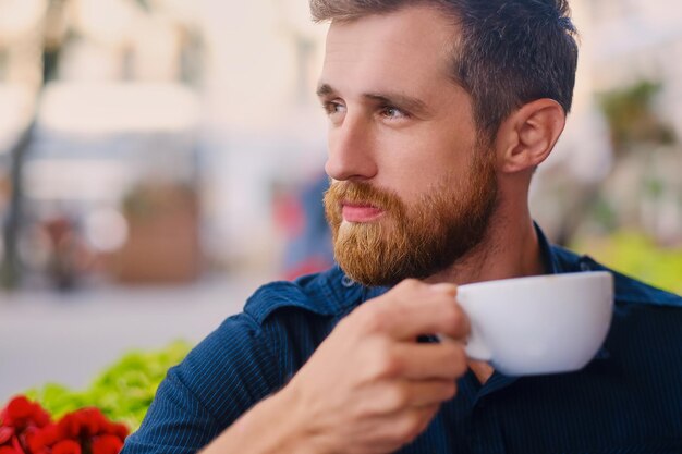 Portrait d'homme décontracté rousse barbu boit du café dans un café dans une rue.
