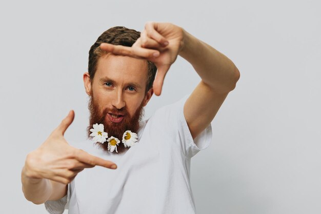 Photo portrait d'un homme drôle dans un t-shirt blanc avec des marguerites de fleurs dans sa barbe sur un lieu de copie de fond blanc isolé concept de vacances et félicitations