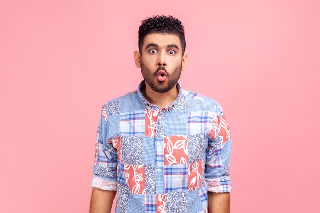 Portrait d'un homme drôle excité en chemise bleue de style décontracté avec des lèvres boudeuses et de grands yeux étonnés l'air surpris et idiot à la caméra se demandait l'expression Studio intérieur tourné isolé sur fond rose