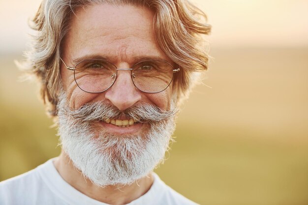 Portrait d'un homme élégant aux cheveux gris et à la barbe qui se tient à l'extérieur sur le terrain à la journée ensoleillée