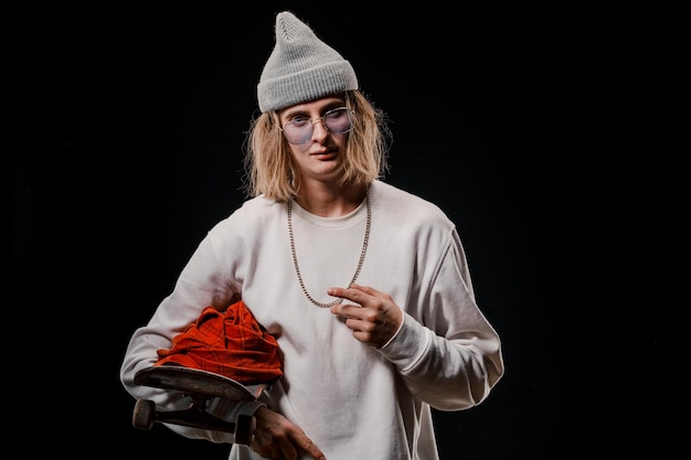 Portrait d'un homme élégant tenant une planche à roulettes en studio. Gros plan d'un skateur souriant posant sur fond noir.