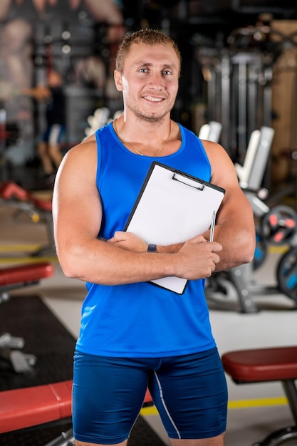Portrait d'un homme un entraîneur personnel tenant un presse-papiers avec un plan d'entraînement dans la salle de sport