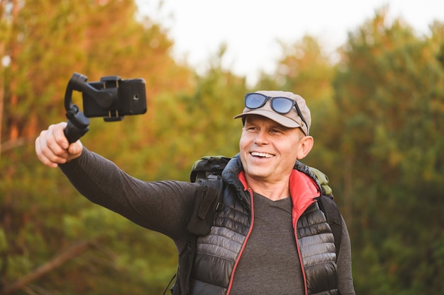 Portrait d'homme faisant de la vidéo et de la photo avec un smartphone et un stabilisateur en forêt