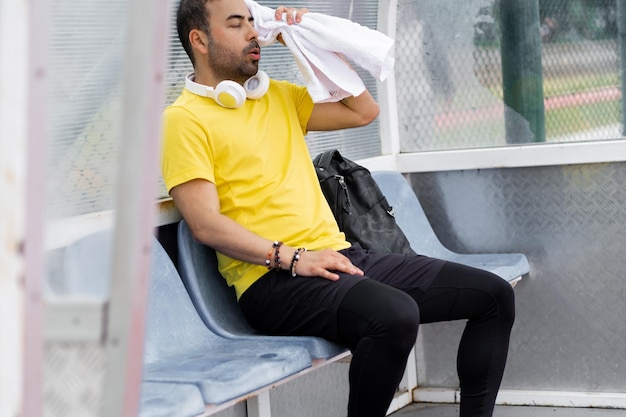 Portrait d'homme fatigué essuyant le visage en sueur avec une serviette assis dans un petit stade arbor après l'entraînement sportif