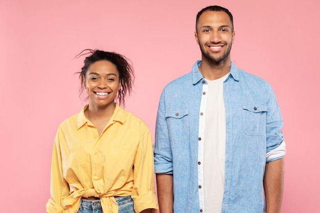 Portrait d'un homme et d'une femme afro-américains gais posant sur fond rose regardant et souriant à la caméra